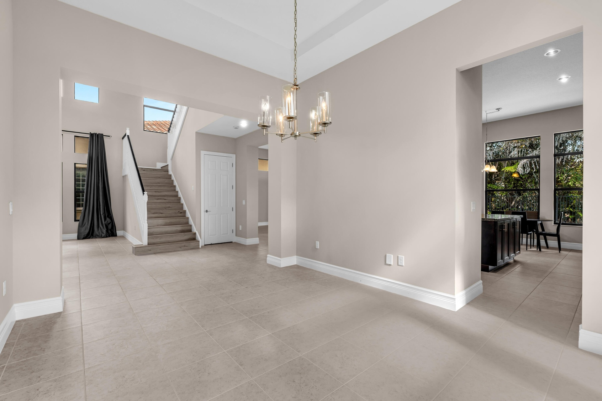 Spacious main living area featuring large format tile flooring, a contemporary chandelier, and a prominent staircase with dark railings