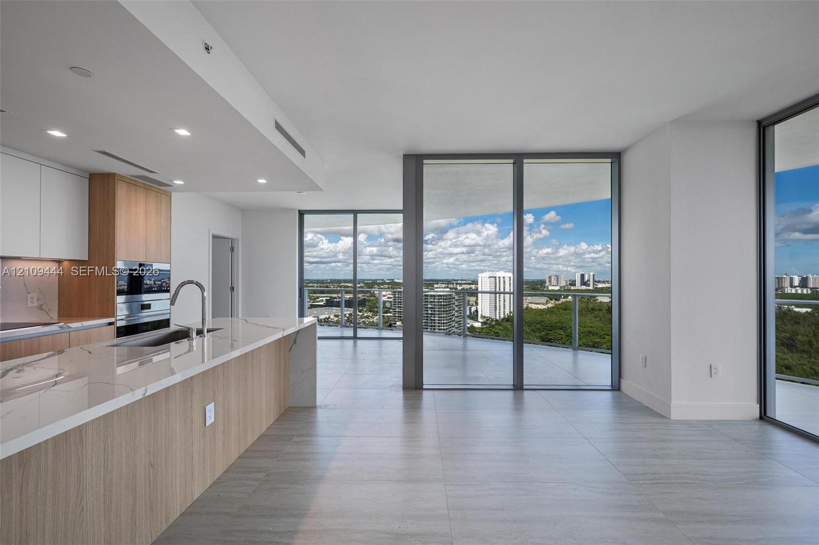 Kitchen featuring wood-finish cabinetry, stone countertops, built-in double ovens, and expansive floor-to-ceiling glass panel doors opening to a wrap-