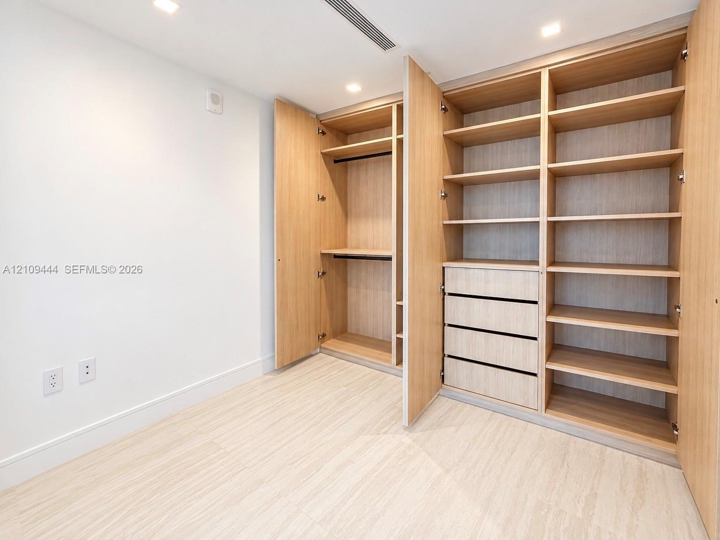 Custom built-in closet featuring light wood-finish shelving, hanging rods, and integrated drawers with recessed lighting and light wood-finish floorin