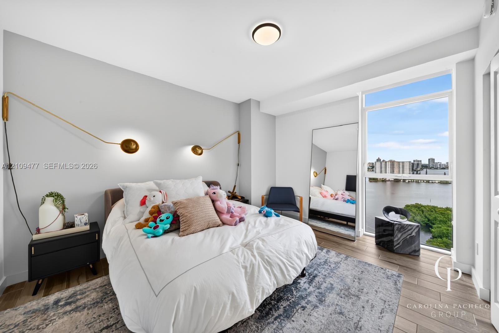 Floor-to-ceiling windows with water backdrop, wood-finish flooring, and dual brass-finish wall-mounted light fixtures