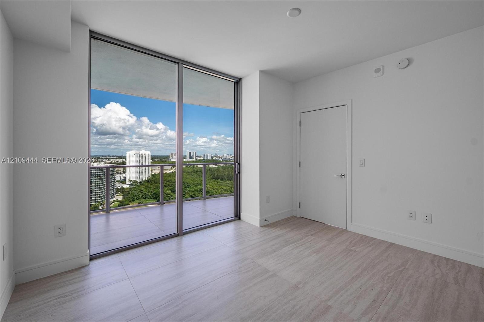 Floor-to-ceiling glass sliding doors, private balcony, wood-finish flooring, and neutral wall palette
