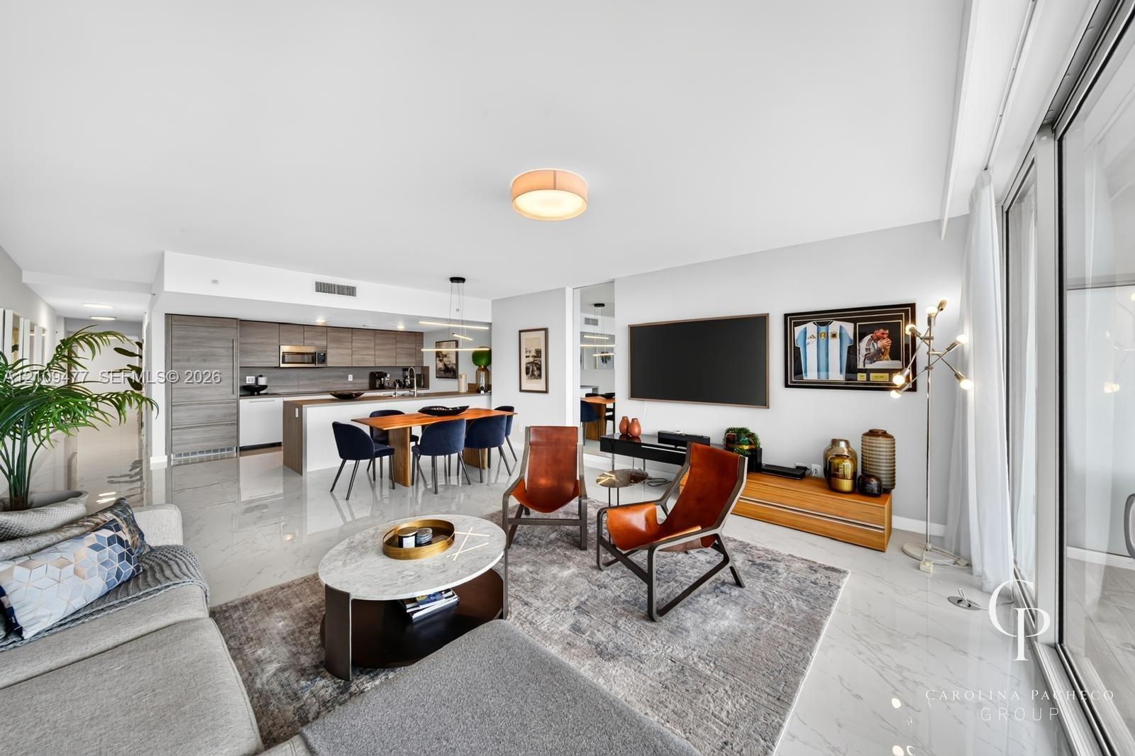 Open-concept interior featuring light-toned flooring, modern kitchen cabinetry with a central island, recessed lighting, and floor-to-ceiling glass sl