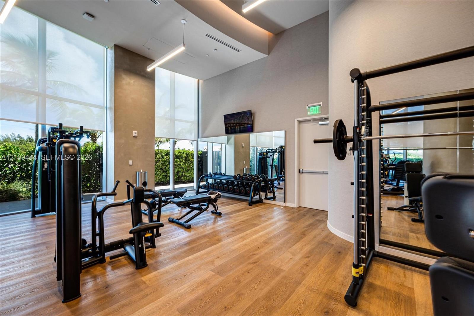 Fitness center featuring floor-to-ceiling windows, wood-finish flooring, high ceilings with recessed lighting, and full-wall mirrors