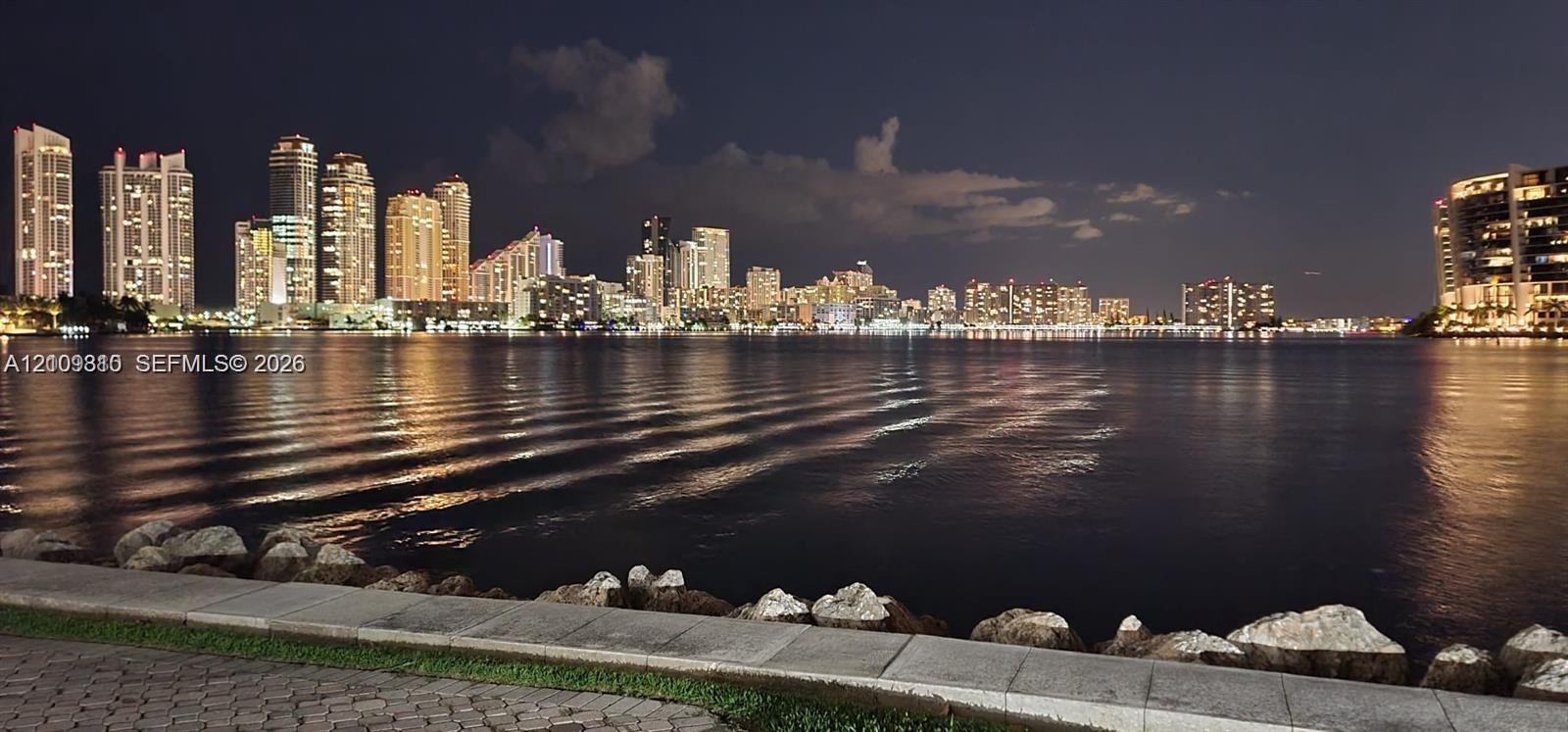 Waterfront property featuring a stone-paved promenade, natural rock bulkhead, and skyline backdrop