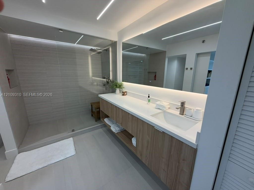 Floating wood-finish vanity with a white countertop and integrated sink, frameless glass walk-in shower with horizontal tile wall detailing, and a lar