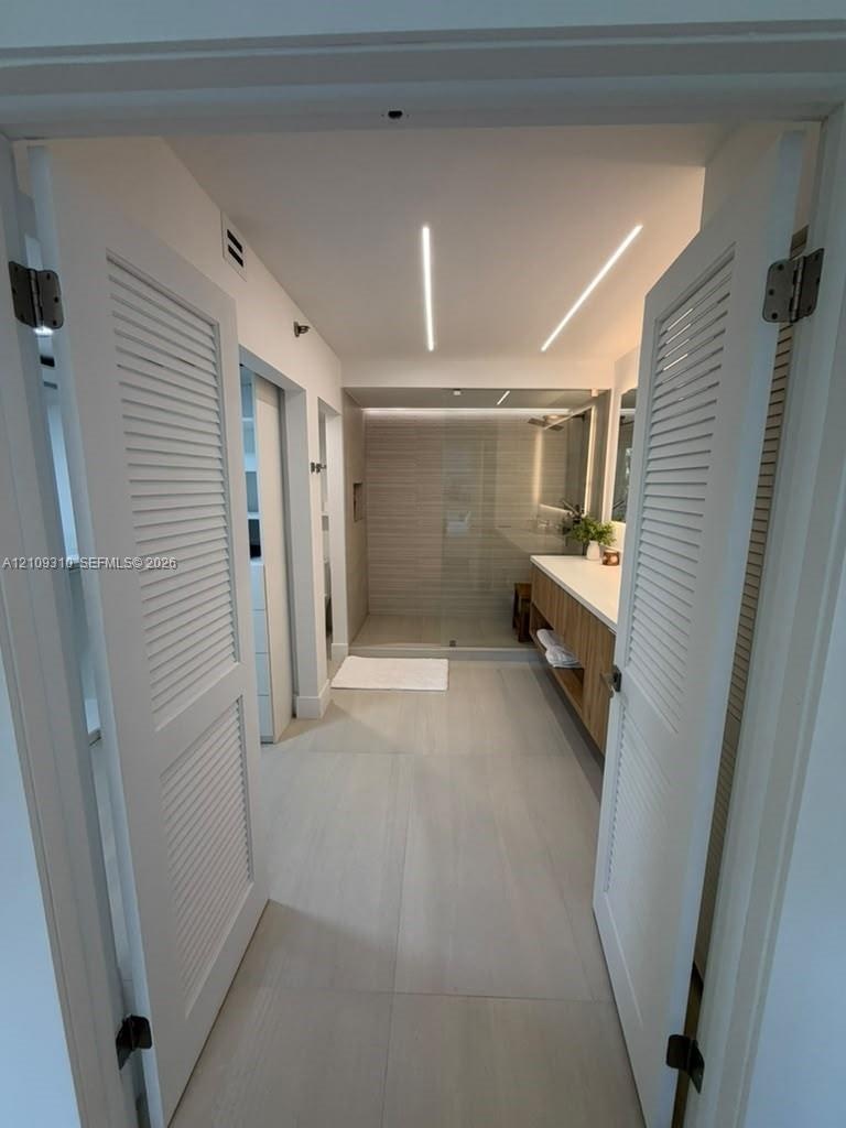 Bathroom featuring dual louvered doors, recessed linear ceiling lighting, floating wood-finish vanity with countertop, and a walk-in glass-enclosed sh