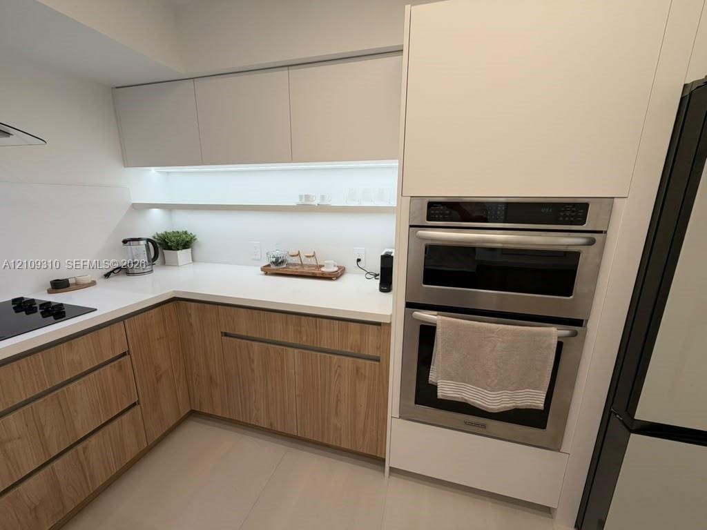 Kitchen featuring two-tone cabinetry with wood-finish lower units, white upper cabinets, white solid-surface countertops, integrated under-cabinet lig