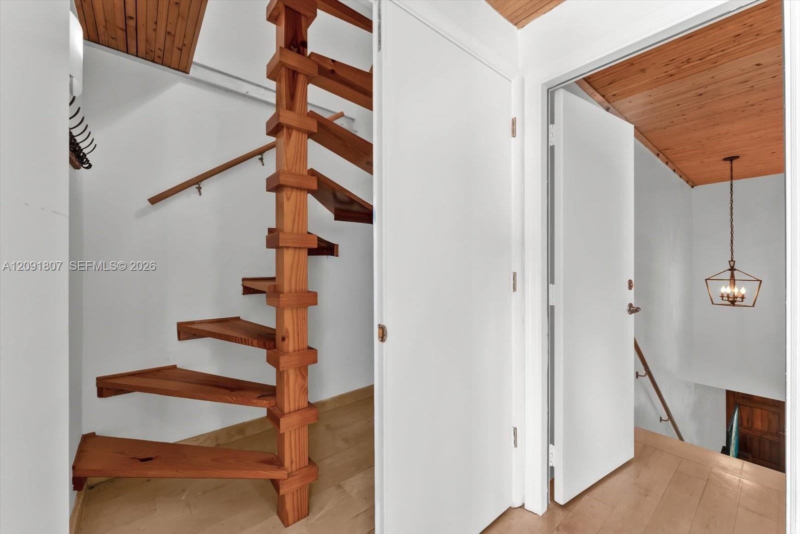 Custom wooden spiral staircase with central support post, wood-finish flooring, planked wood ceilings, and geometric metal pendant lighting
