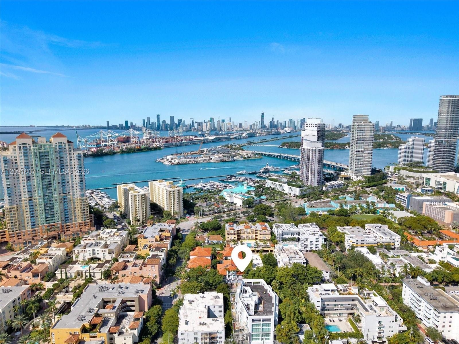 Aerial perspective of the coastal cityscape featuring a prominent skyline, expansive waterway, marinas, high-rise architecture, and mature canopy foli