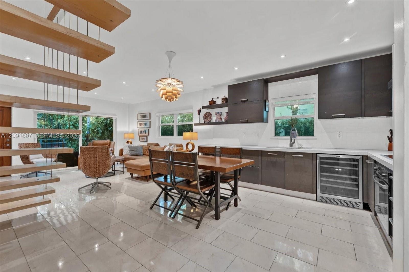 Open-concept kitchen and living area featuring a floating staircase with wood treads, high-gloss cabinetry, built-in wine refrigeration, large-format 