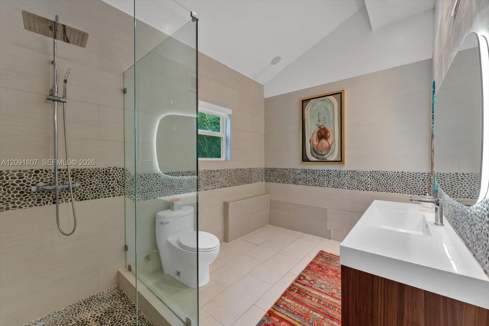 Bathroom featuring a glass-enclosed shower with pebble stone flooring and wall accents, a wood-finish vanity with a rectangular sink, wall-mounted ill