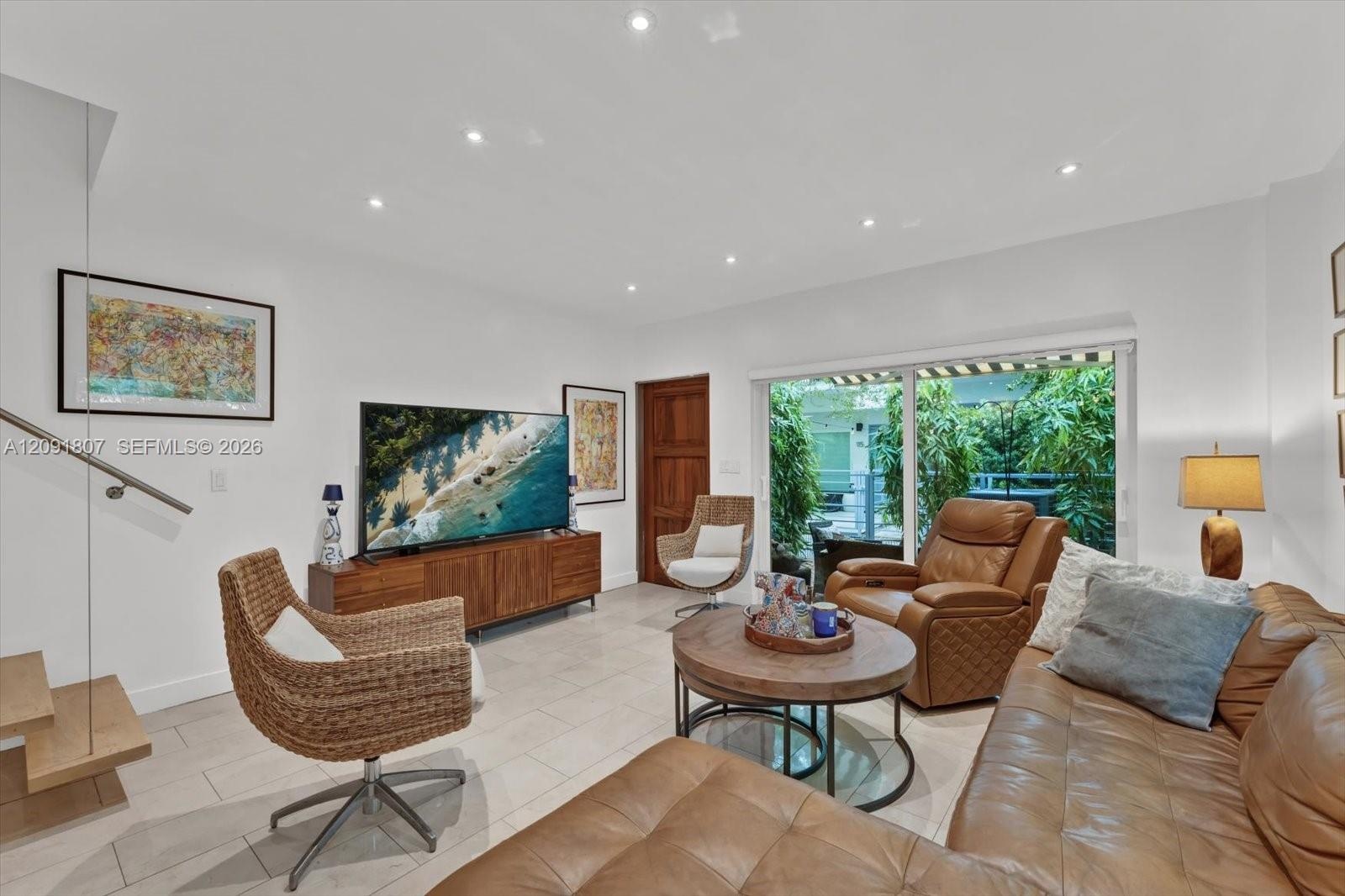 Large-format tile flooring, recessed ceiling lighting, sliding glass door with exterior access, and a floating wood-tread staircase with a glass panel