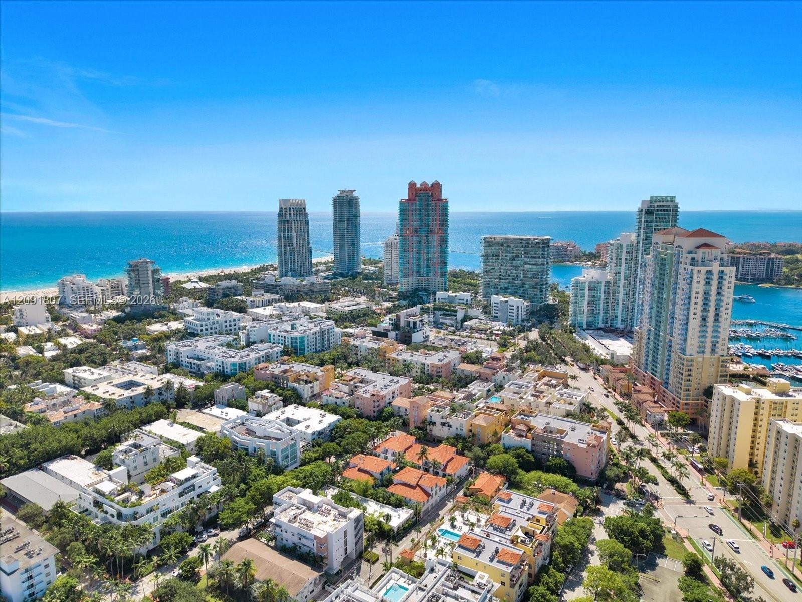 Aerial perspective of a coastal urban landscape featuring high-rise towers, proximity to the shoreline, a marina, and dense metropolitan infrastructur