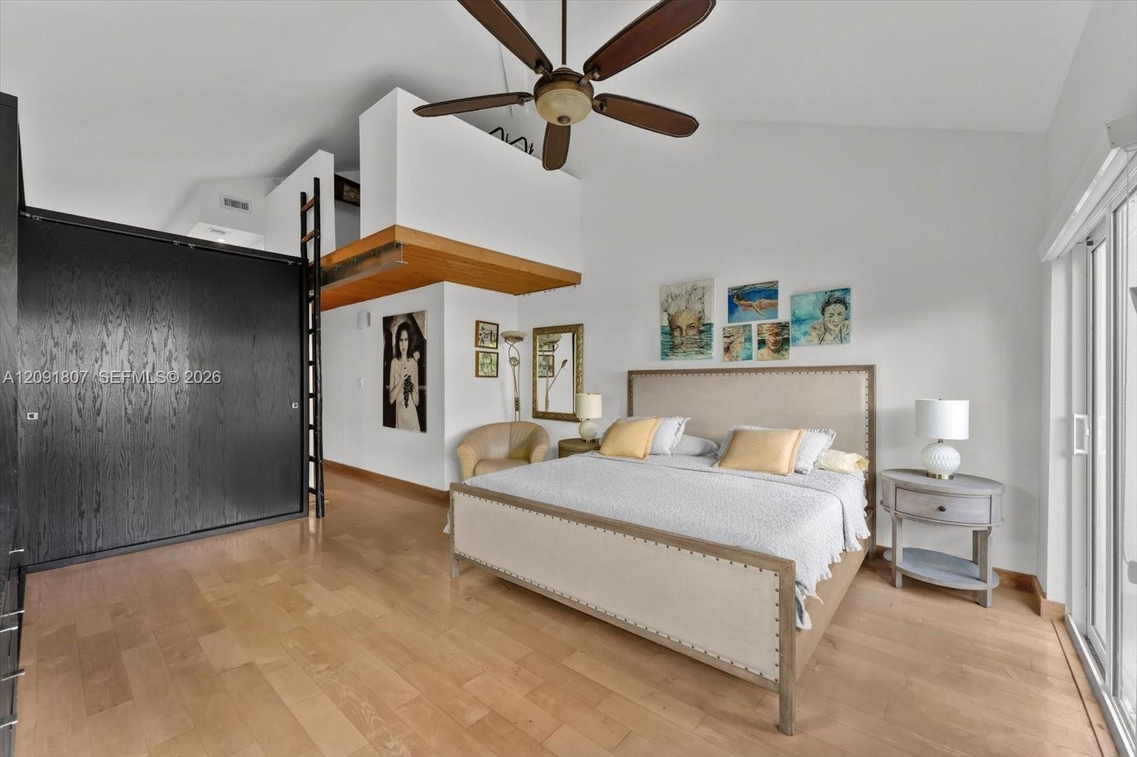 Vaulted ceilings featuring a prominent ceiling fan, wood-finish flooring, floor-to-ceiling dark-finish cabinetry, a built-in ladder, and sliding glass