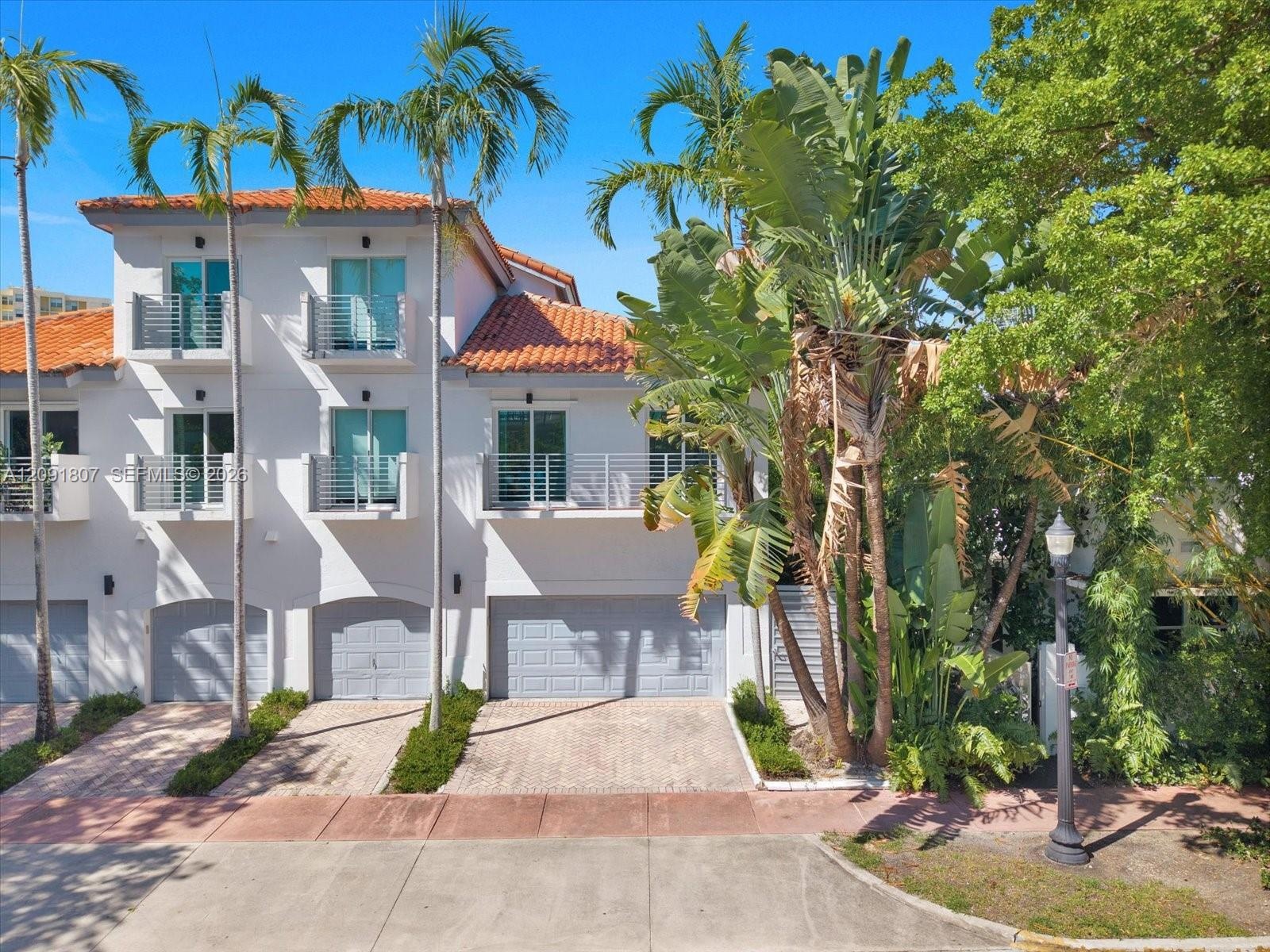 Three-story exterior featuring a terracotta tile roof, white stucco facade, multiple private balconies with metal railings, and attached multi-car gar