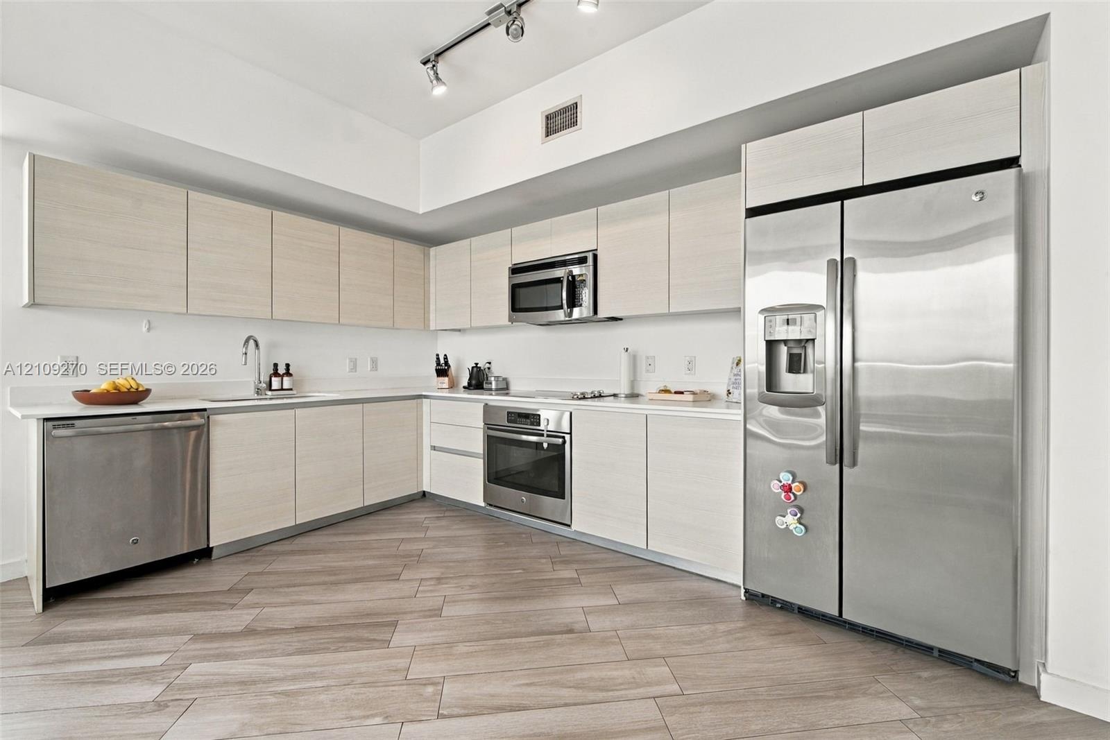 Kitchen featuring flat-panel cabinetry, light-toned countertops, stainless steel appliances, and plank-style flooring with integrated track lighting