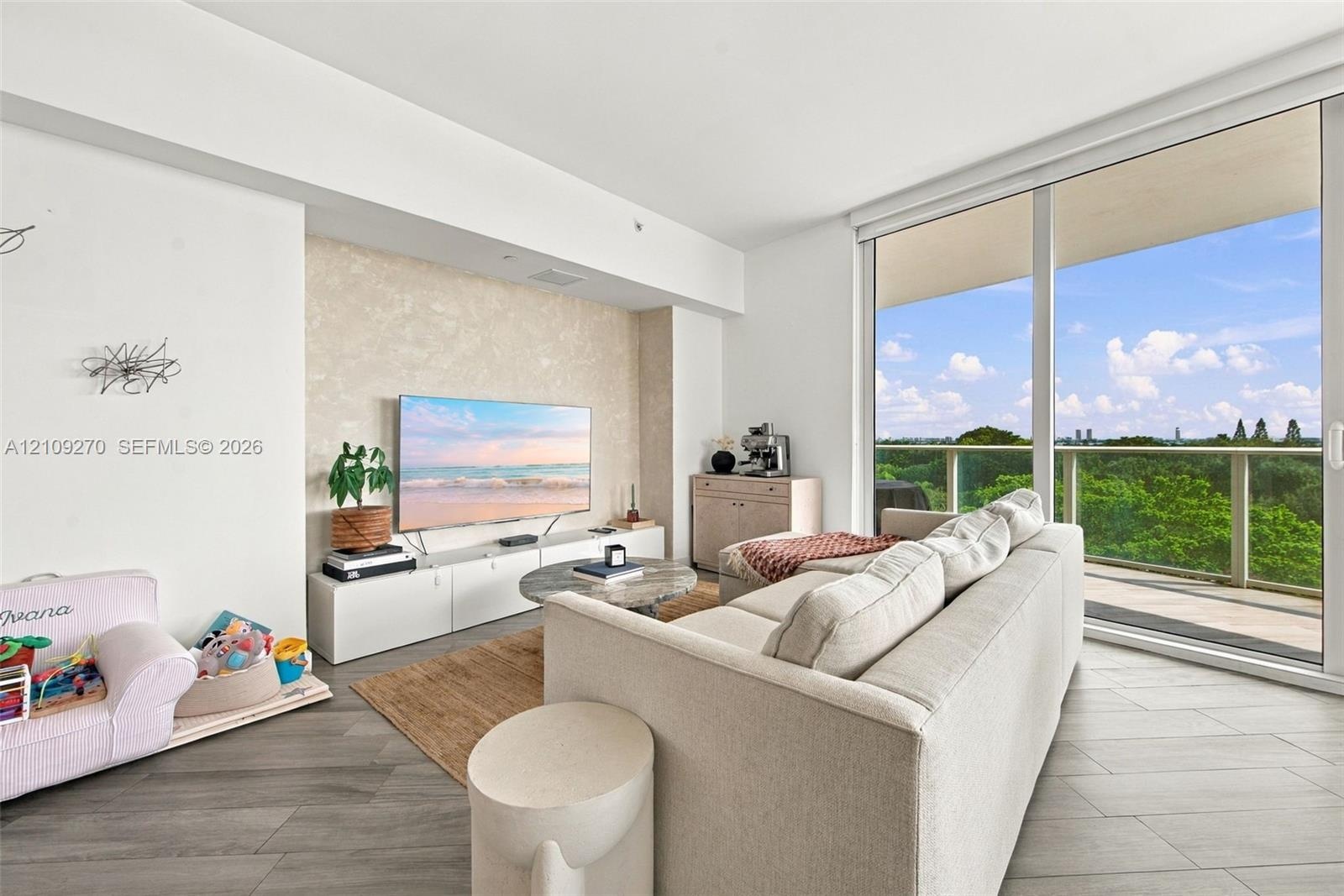 Floor-to-ceiling sliding glass doors, spacious balcony with glass railing, wood-finish flooring, and a textured accent wall