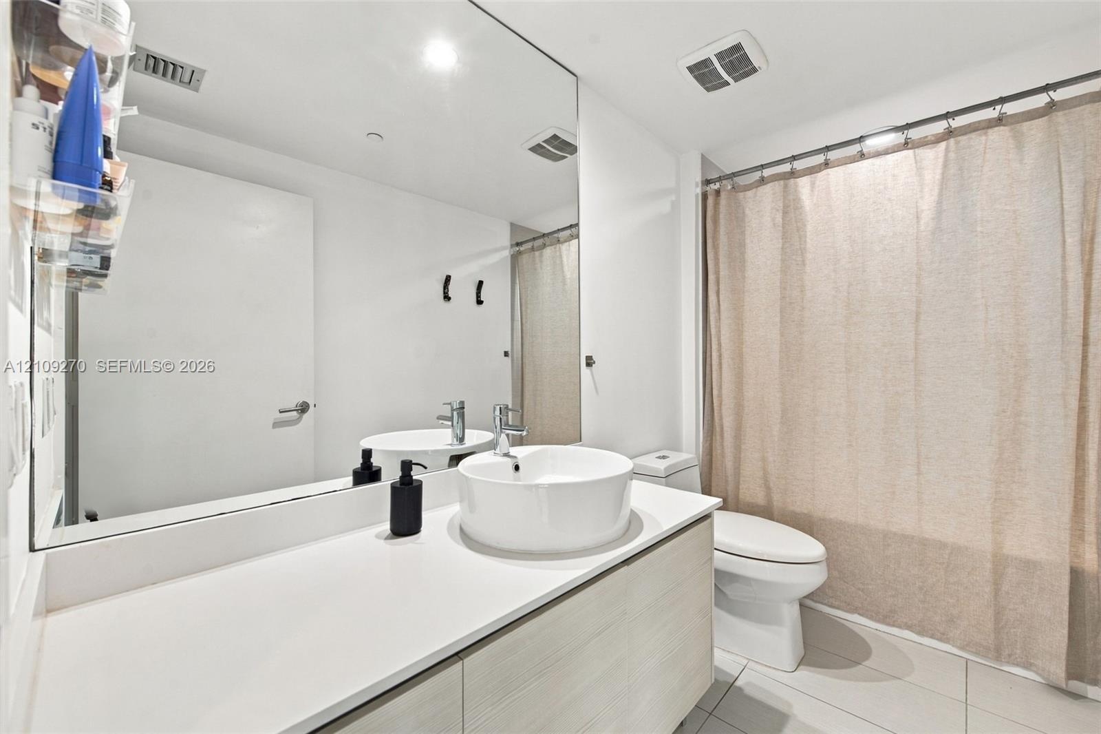Modern floating vanity with a light wood-finish cabinet, rectangular surface-mounted sink, and wide-format wall mirror featuring a polished chrome fau