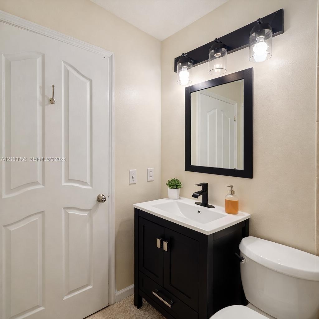 Dark-finished vanity with a white countertop and integrated sink, matte black faucet, framed mirror, and three-light wall-mounted fixture