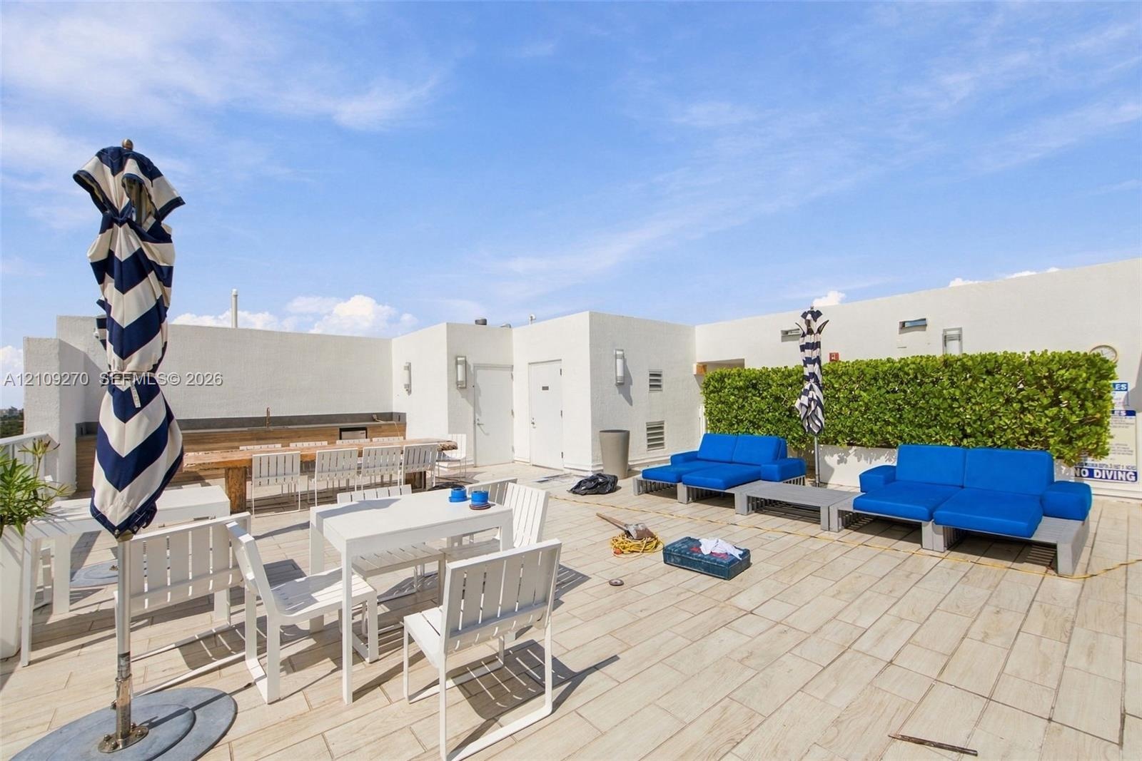 Rooftop terrace featuring light-toned tile flooring, integrated perimeter hedge, stucco wall finishes, and built-in outdoor kitchen structure with att