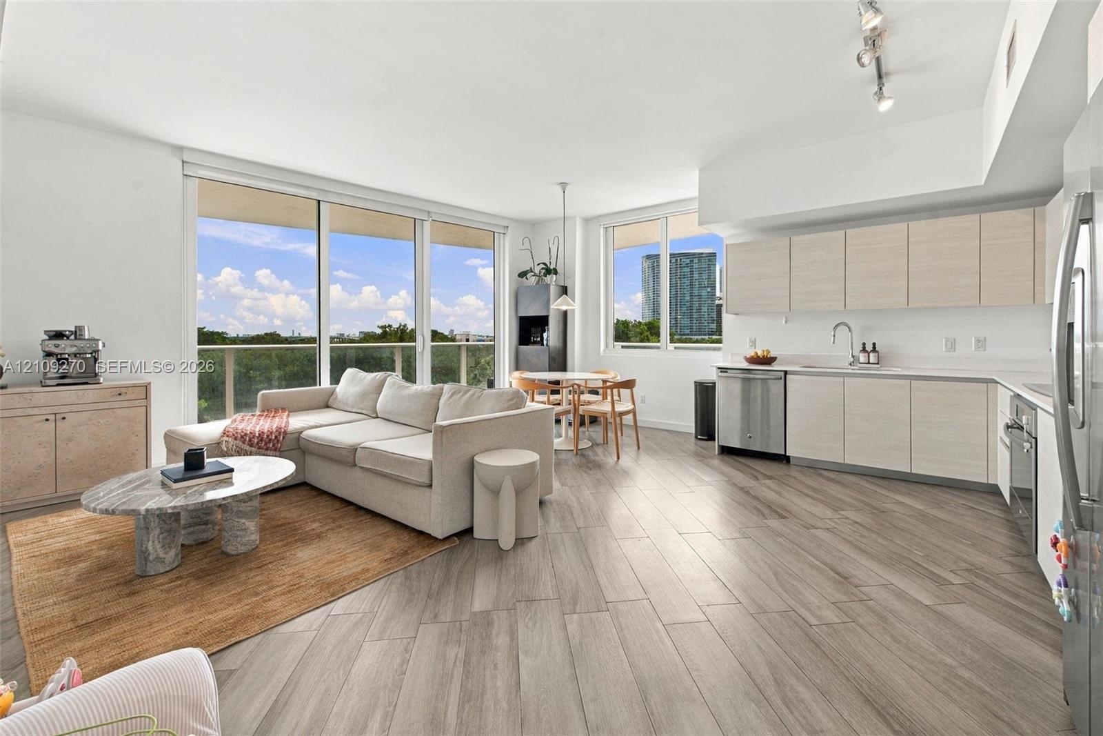 Open-concept main living area featuring wood-finish flooring, floor-to-ceiling glass sliding doors, flat-panel cabinetry, stainless steel appliances, 