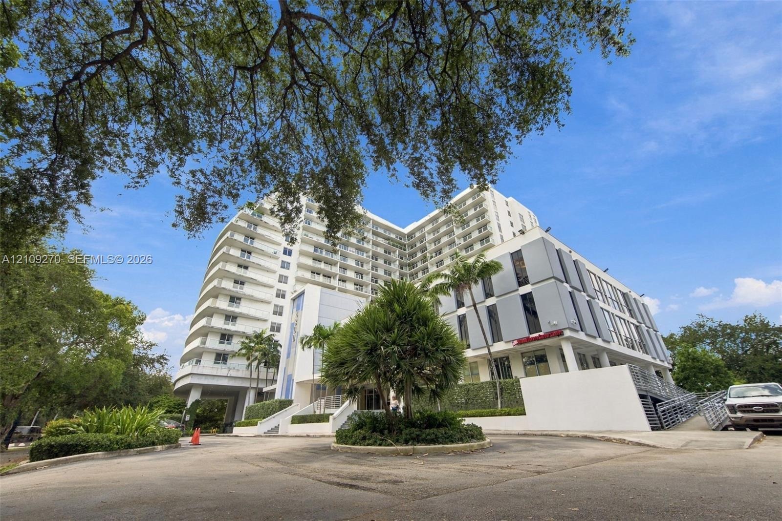 Multi-story building exterior featuring a white concrete facade, recessed private balconies, and panelized metal cladding