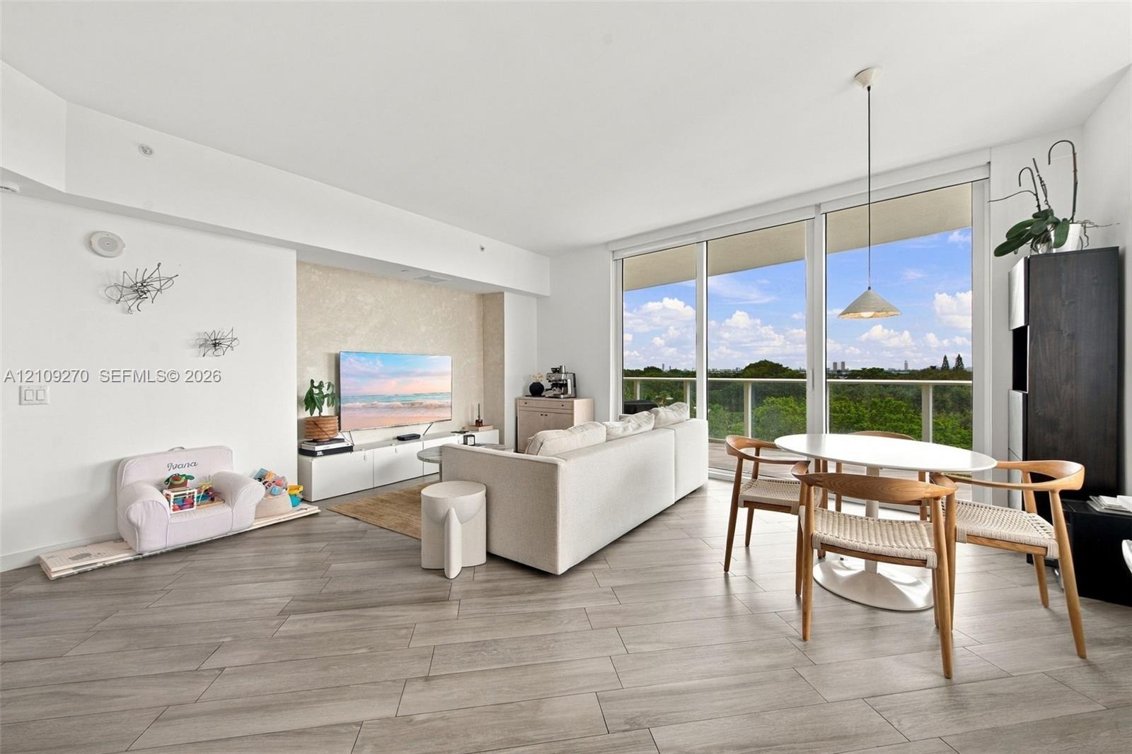 Open-concept living space featuring wood-finish flooring, floor-to-ceiling glass sliding doors, a balcony, and a recessed accent wall with built-in me