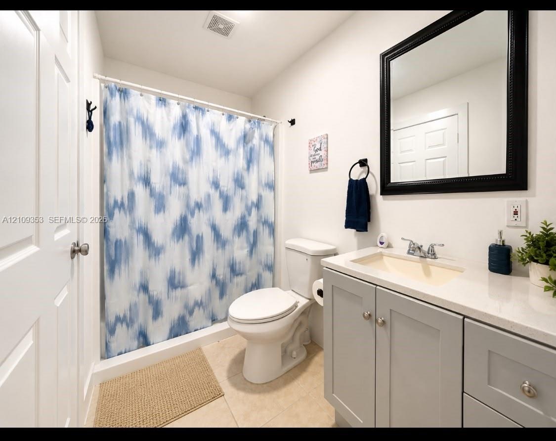 Bathroom featuring a vanity with light gray shaker-style cabinetry, a solid surface countertop, an integrated rectangular sink, a black-framed mirror,