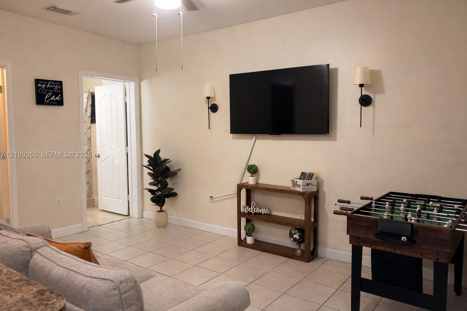 Neutral-toned interior featuring ceramic tile flooring, dual wall-mounted light fixtures, and a six-panel interior door