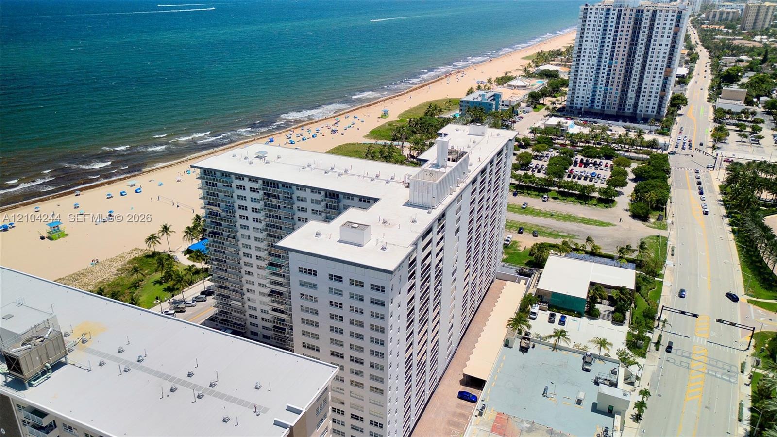 High-rise structure featuring exterior balconies, a flat roofline, and covered surface parking, situated along a coastal coastline