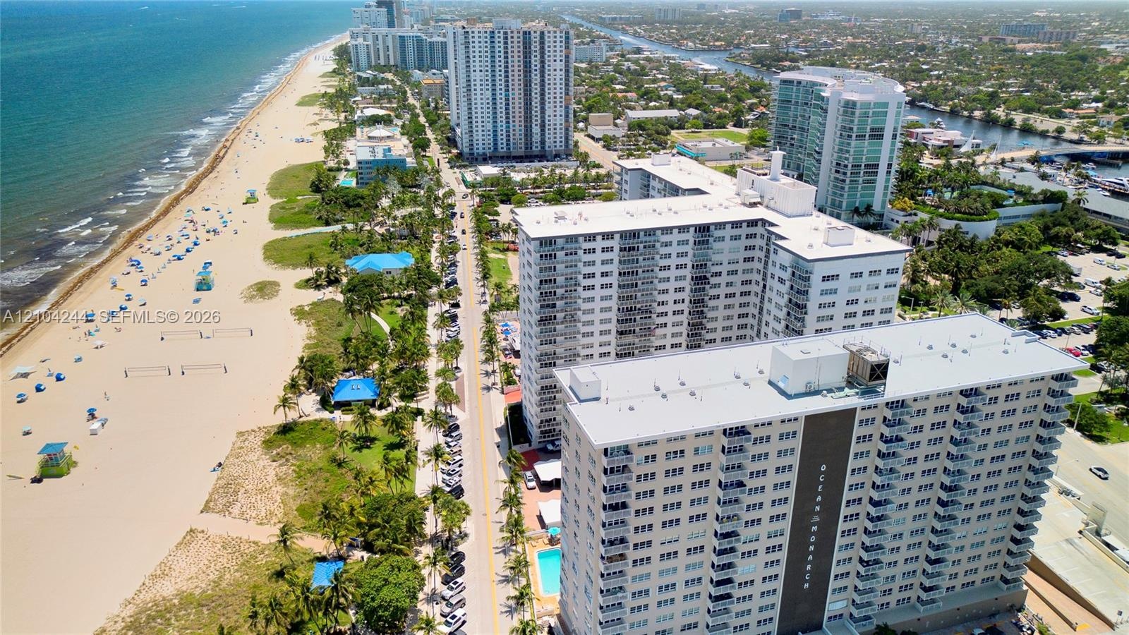 Aerial perspective of high-rise building with balcony access, positioned along the coastline featuring sandy shoreline and oceanfront proximity