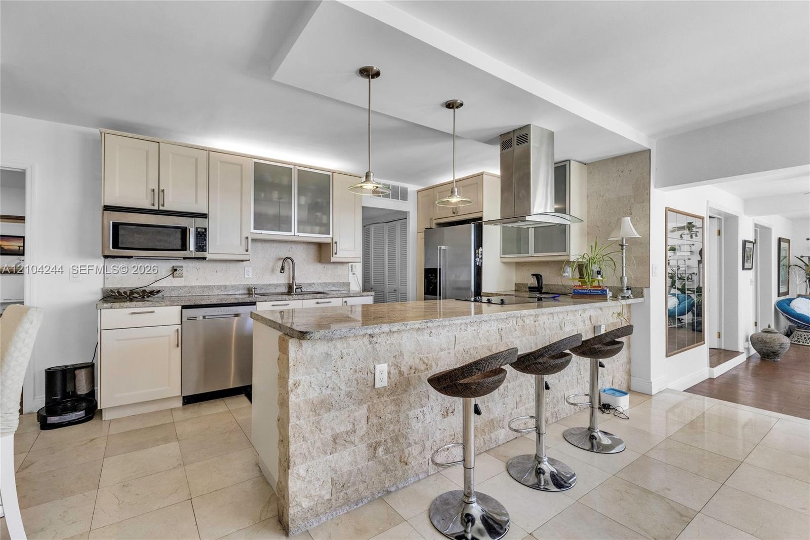 Kitchen featuring stone-clad breakfast bar, stone countertops, stainless steel appliances, cabinet-fronted upper storage with glass inserts, and two p