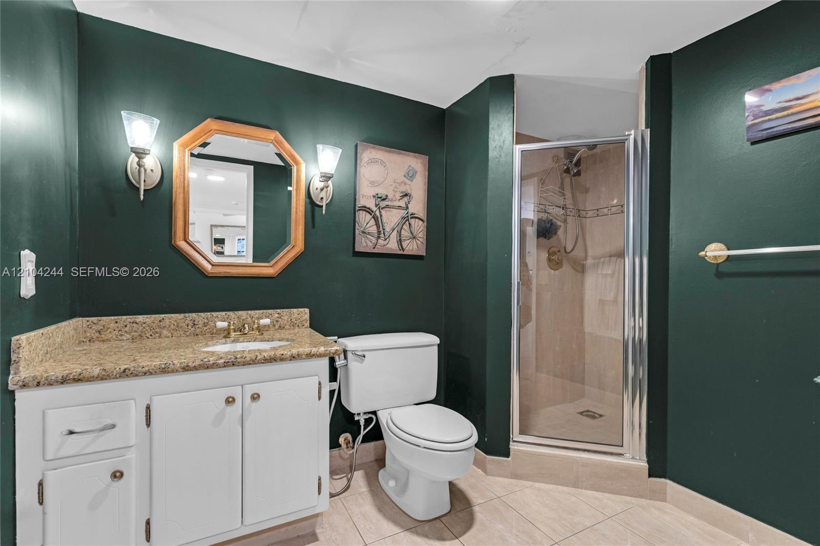 Bathroom featuring a white vanity cabinet with stone-finish countertop, undermount sink, dual wall-mounted light fixtures, and a glass-enclosed shower