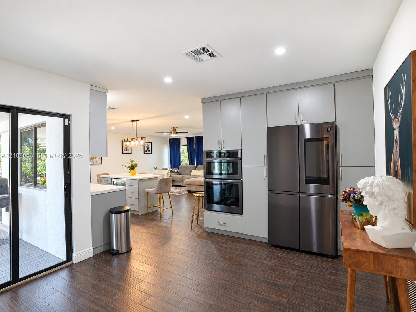 Kitchen featuring full-height light gray cabinetry, built-in stainless steel double wall ovens, a multi-door refrigerator, a center island, and wood-f