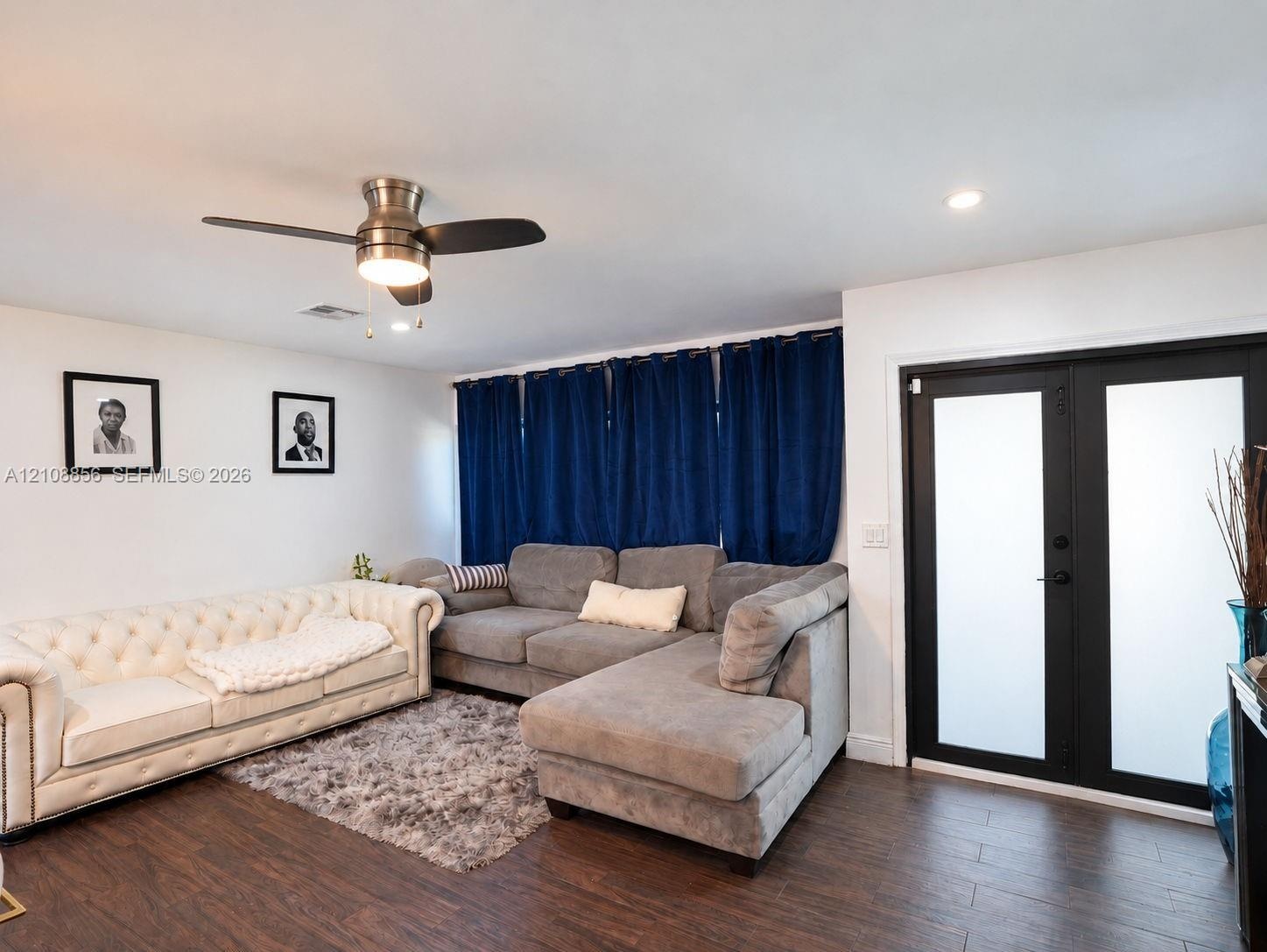 Wood-finish flooring, brushed metal ceiling fan with integrated lighting, and black-framed double doors with frosted glass panels