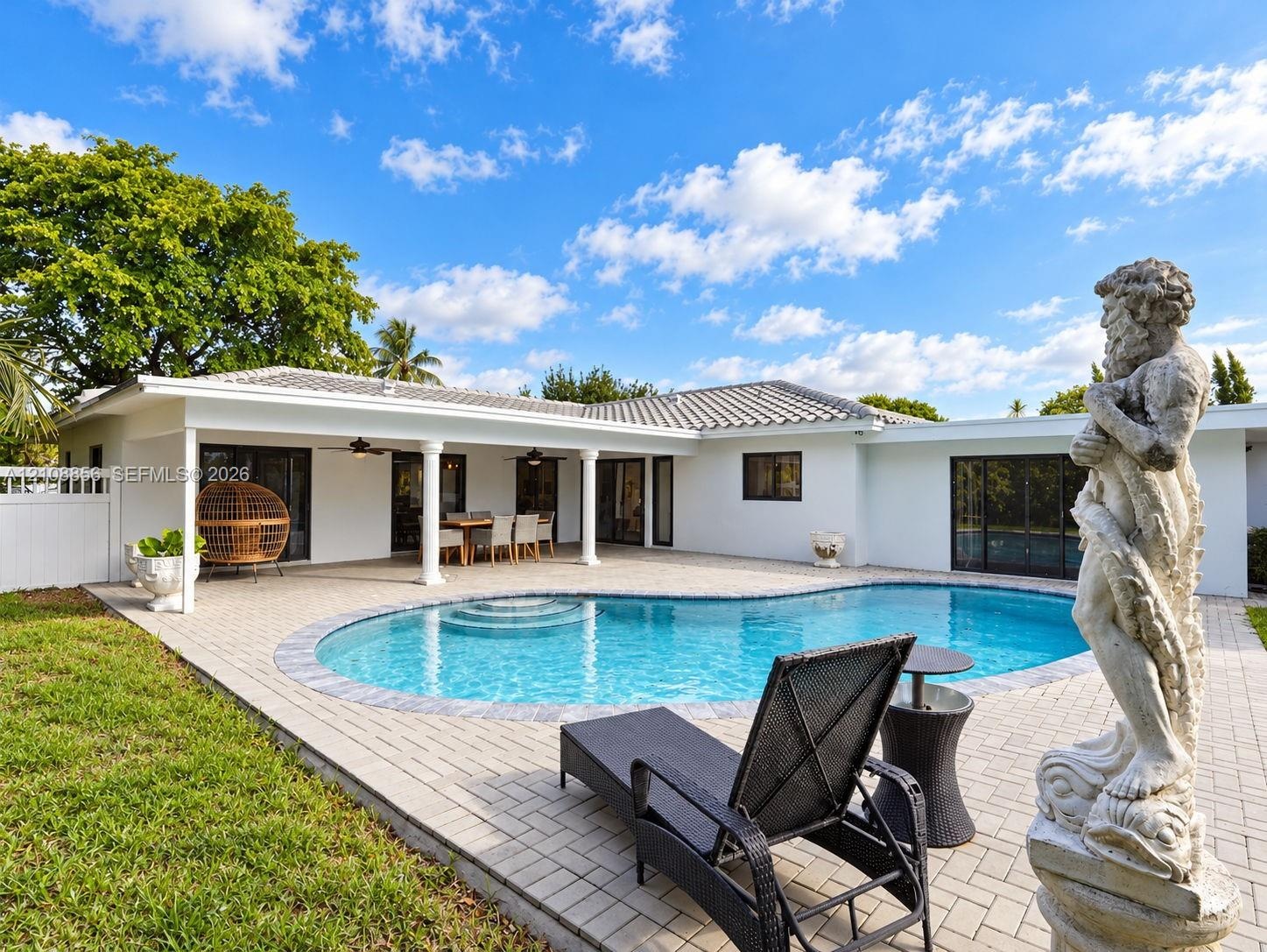 Backyard featuring a curved inground pool, expansive paver patio, covered porch with column supports, and manicured lawn
