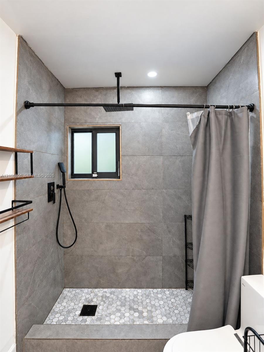 Walk-in shower featuring large-format grey tile surround, hexagonal floor tiling, a ceiling-mounted rainfall showerhead, and matte black plumbing fixt