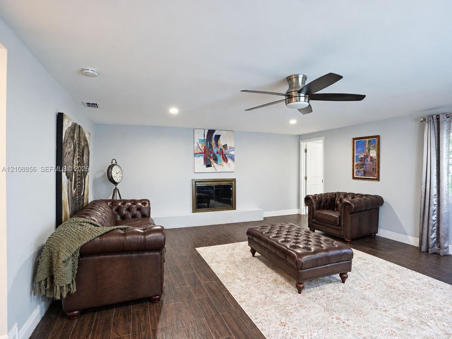 Living space featuring wood-finish flooring, a flush-mounted ceiling fan, recessed lighting, and a fireplace with a metallic surround