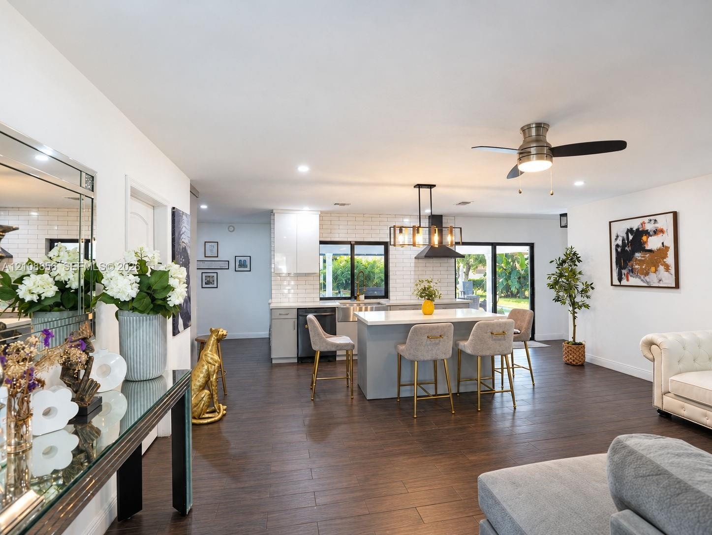 Open-concept kitchen featuring an island with stone countertop, white subway tile backsplash, farmhouse-style sink, dark cabinetry, and wood-finish fl