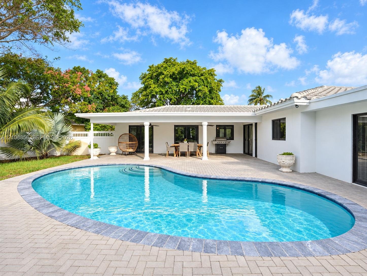 Covered patio with architectural columns, stone-paver pool deck, and freeform swimming pool featuring a decorative stone border