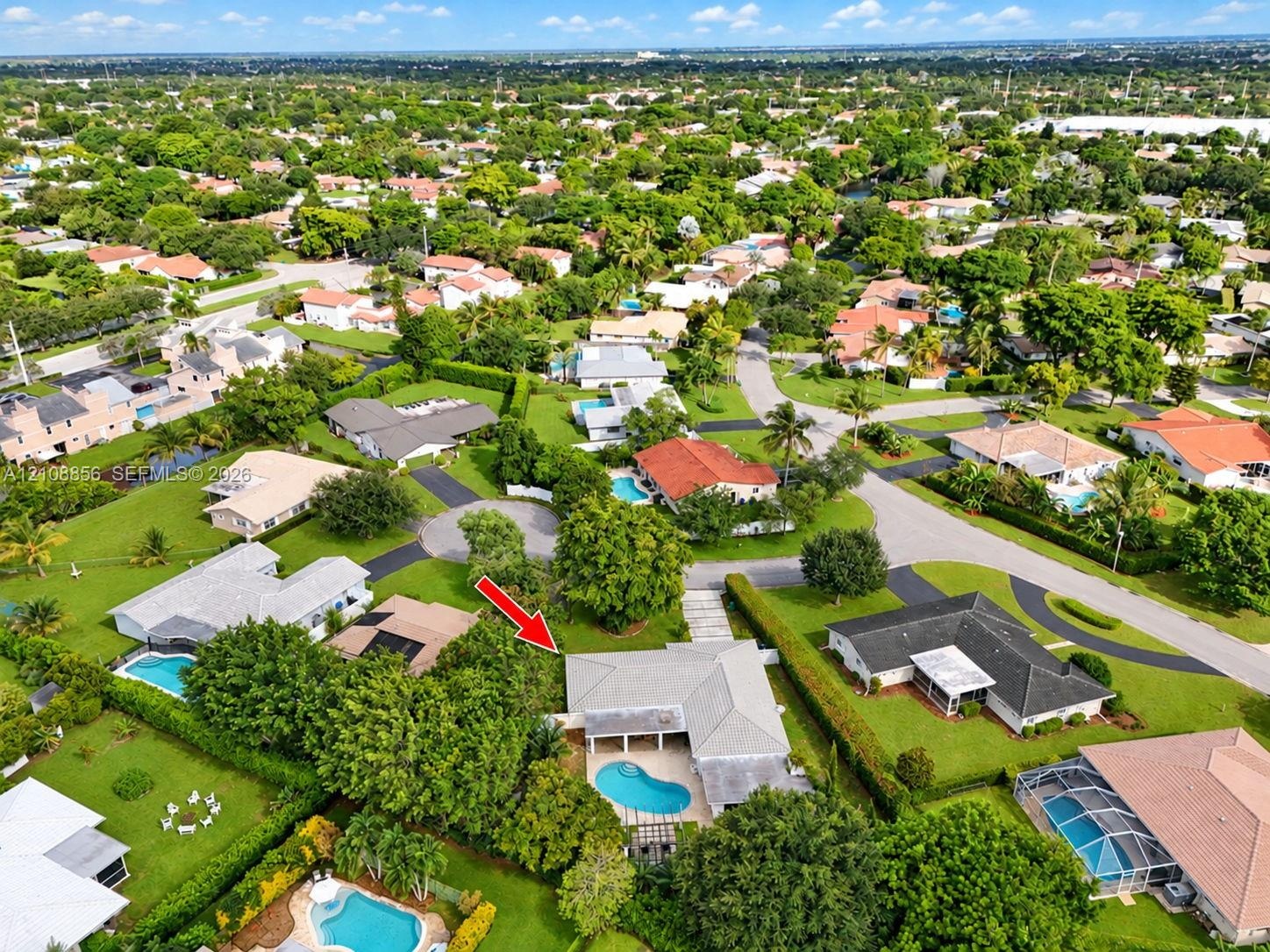 Aerial perspective of a single-story residence featuring a private swimming pool, concrete patio, hipped roofline, and mature landscaping