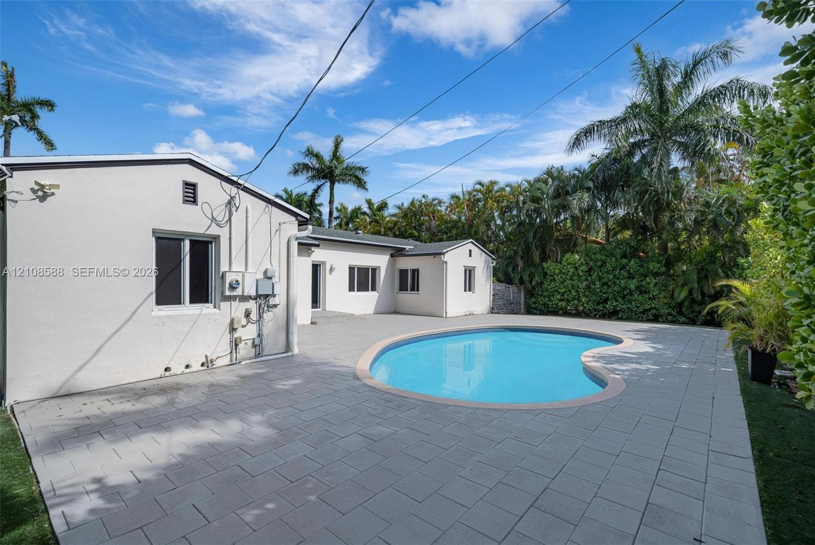 Stucco exterior residence featuring an in-ground kidney-shaped pool and expansive stone-paver patio