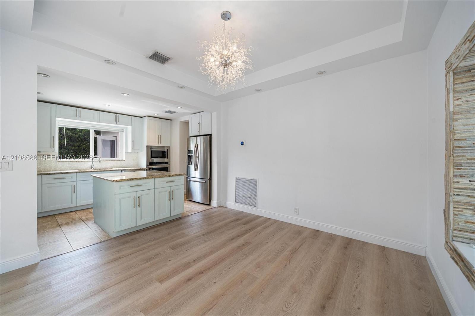 Tray ceiling with recessed lighting, central crystal-style chandelier, wood-finish flooring, kitchen island with stone countertop, and stainless steel