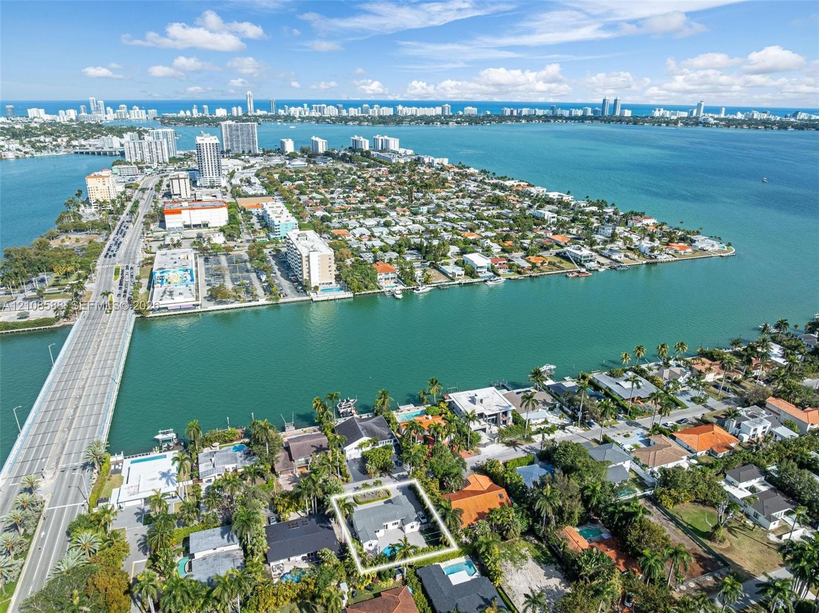 Aerial perspective of a coastal residential property featuring a swimming pool, mature palm trees, and perimeter landscaping