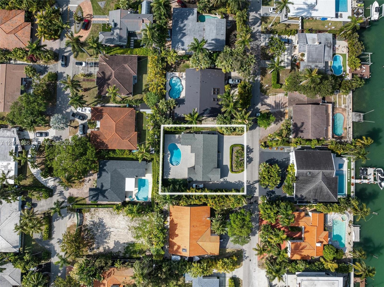 Aerial perspective of a property featuring an in-ground swimming pool, concrete patio, paved driveway, and mature landscaping
