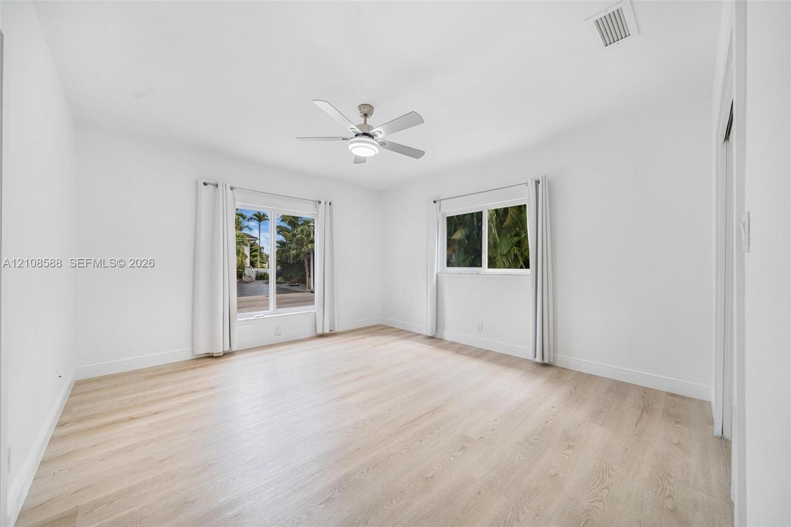 Room featuring light-toned wood-finish flooring, dual windows with exterior foliage, and a ceiling-mounted light fixture with a multi-blade fan