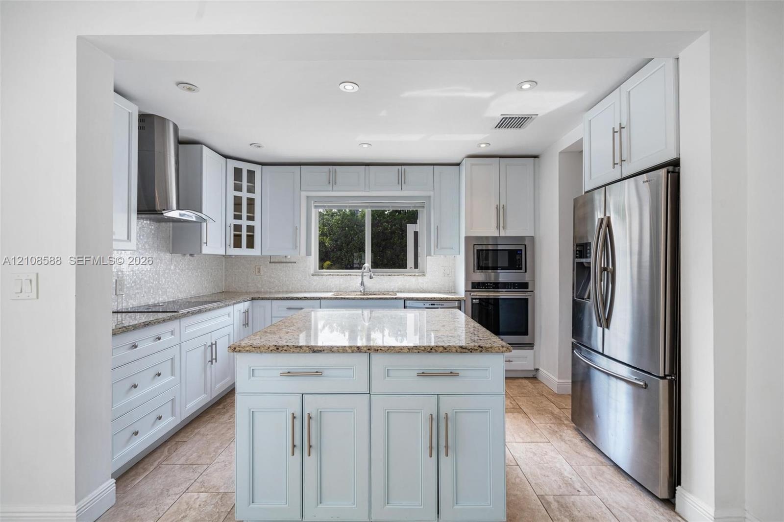 Kitchen featuring white shaker cabinetry, central island with stone countertop, stainless steel appliances, mosaic tile backsplash, and ceramic tile f
