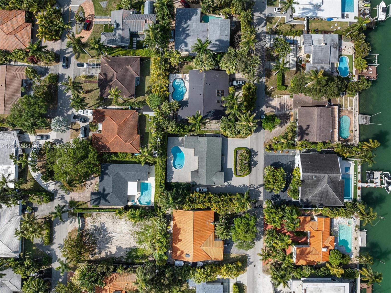 Aerial perspective of a coastal residential neighborhood featuring waterfront properties, private swimming pools, paved driveways, and mature landscap