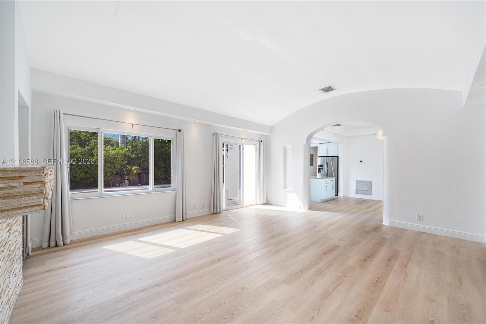 Living area featuring wood-finish flooring, a vaulted barrel-style ceiling, arched wall openings, a stacked-stone fireplace surround, and sliding glas