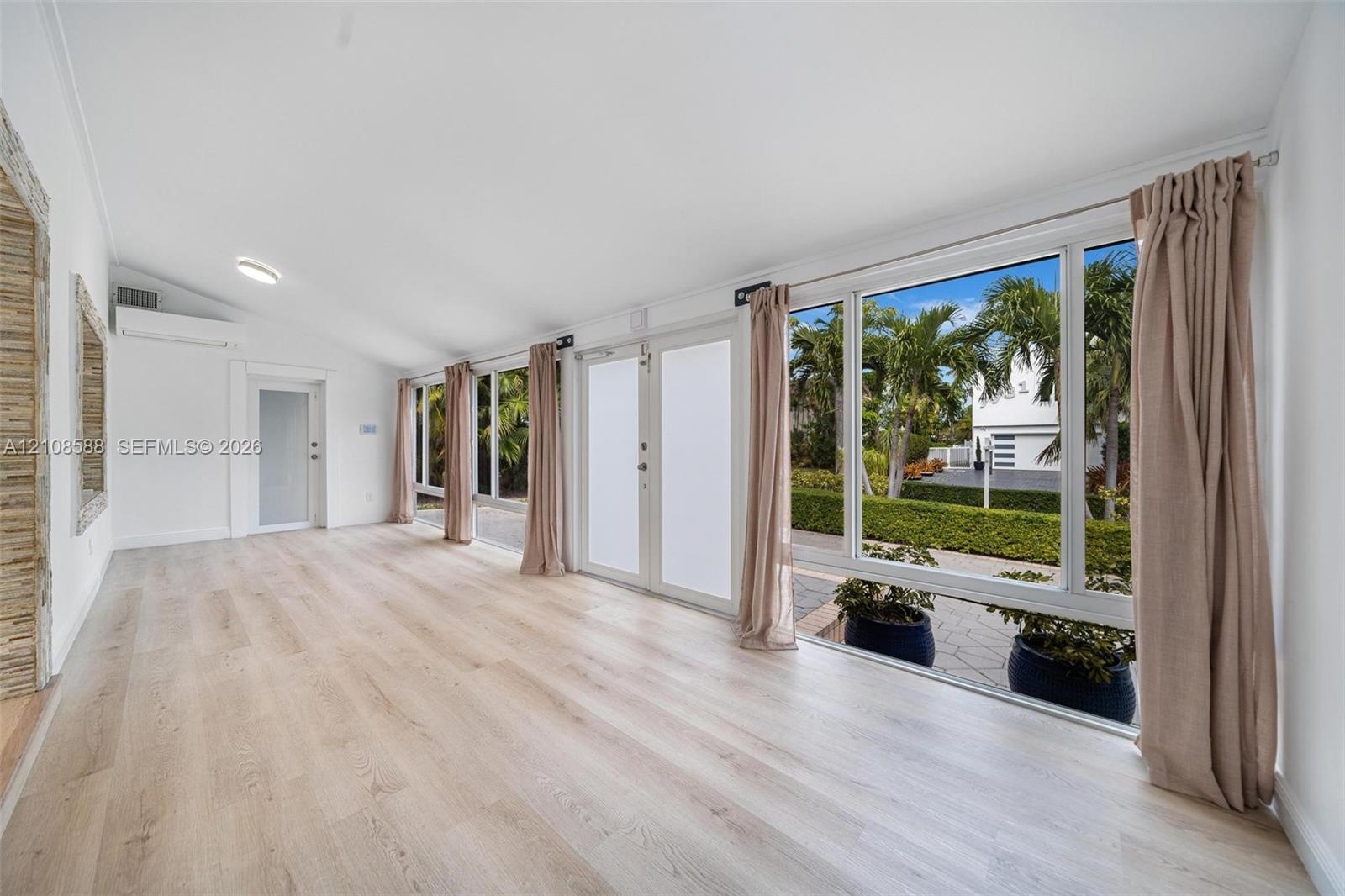 Sun-filled room featuring wood-finish flooring, a vaulted ceiling, floor-to-ceiling windows, and dual glass entry doors